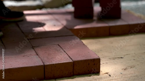 Low angle extreme closeup of person installing brick pavers onto sand base wearing blue gloves. photo