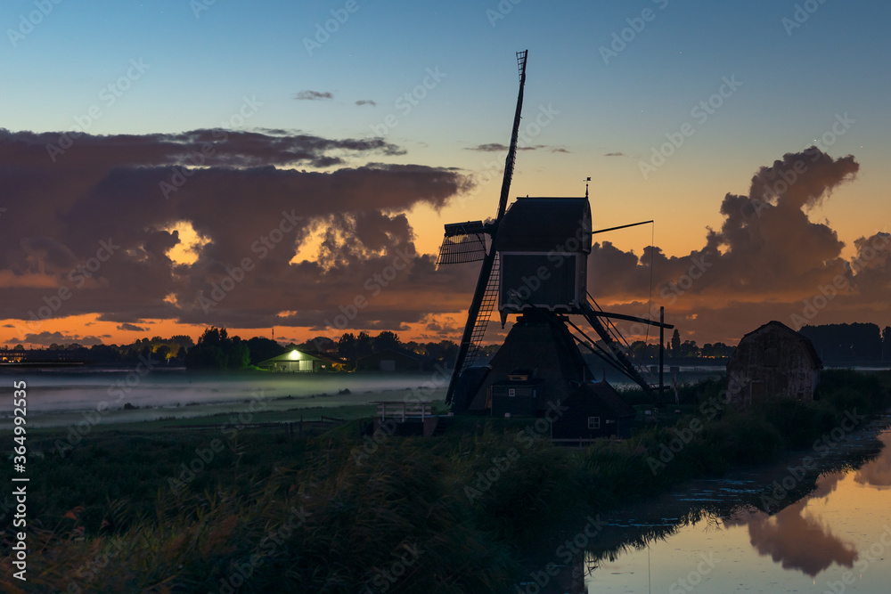 Traditional dutch windmill at sunset with fog over the meadows