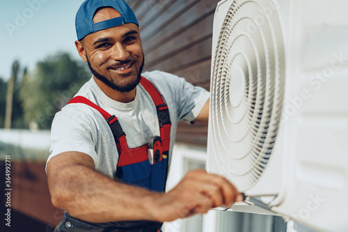 Young black man repairman checking an outside air conditioner unit photo