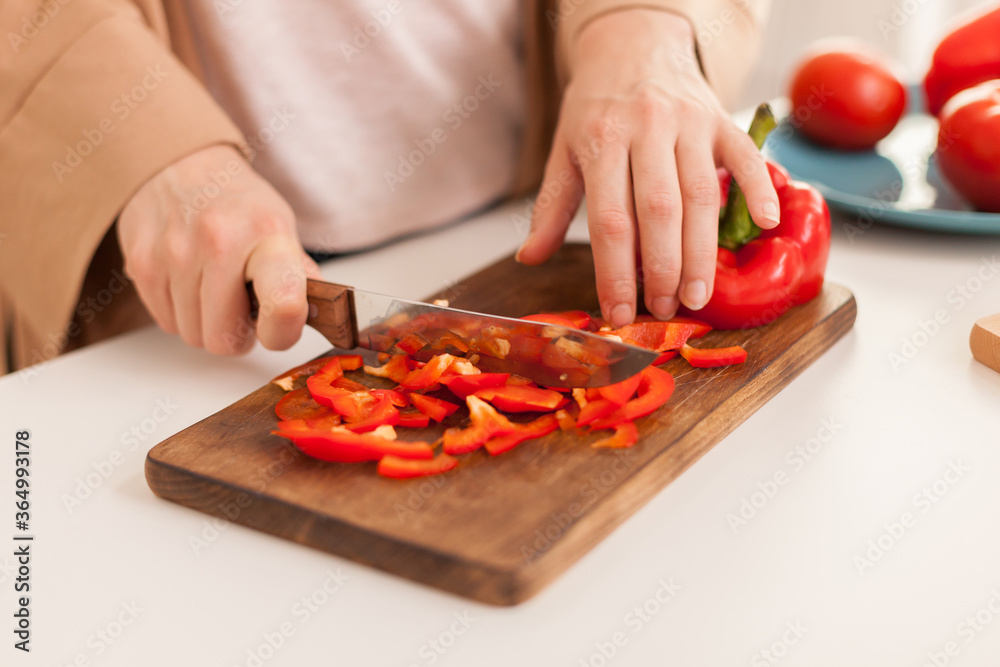 Close up of hand slicing pepper on cutting board in kitchen.