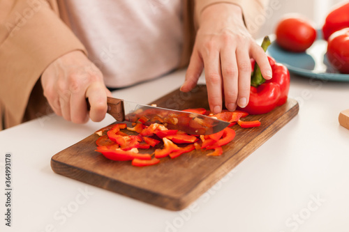 Close up of hand slicing pepper on cutting board in kitchen.
