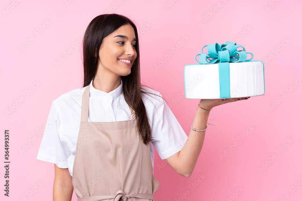 Young woman with a big cake over isolated background with happy expression