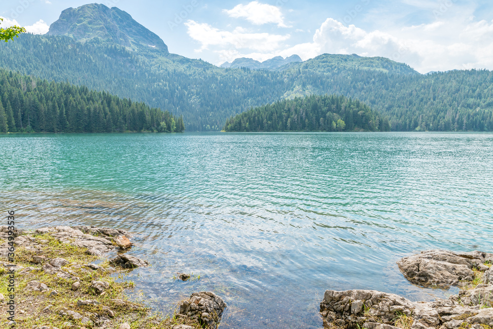 Rocky Black lake shore and opposite bank covered with forest