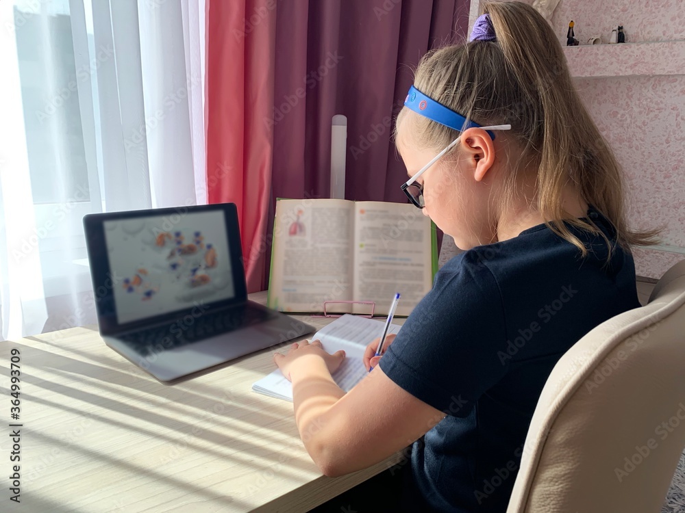 Girl at the table, writes with a pen in a notebook. Home computer training for a schoolboy. A student's desk near the window. Books and notebooks for learning. Girl at the table, writes with a pen in a notebook. Home computer training for a schoolboy. A student's desk near the window. Books and notebooks for learning.