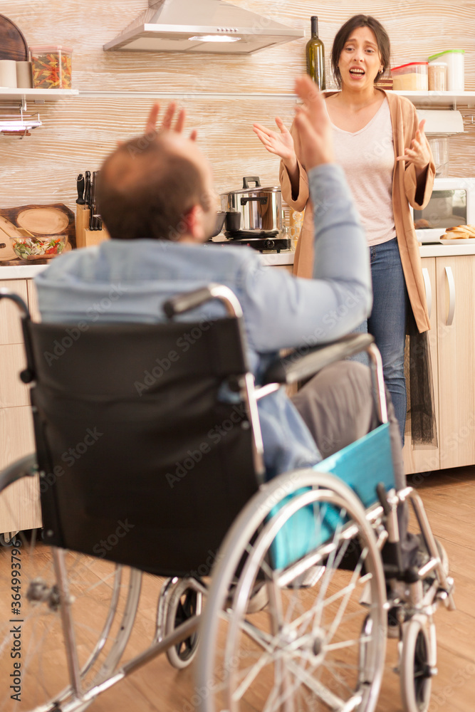 Wife screaming in kitchen to her disabled man in wheelchair while having a disagreement. Disabled paralyzed handicapped man with walking disability integrating after an accident. Wife screaming in kitchen to her disabled man in wheelchair while having a disagreement. Disabled paralyzed handicapped man with walking disability integrating after an accident.