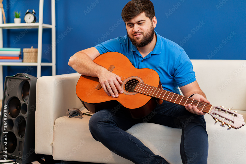 Obraz premium Young man guitar player sitting and performing on a couch
