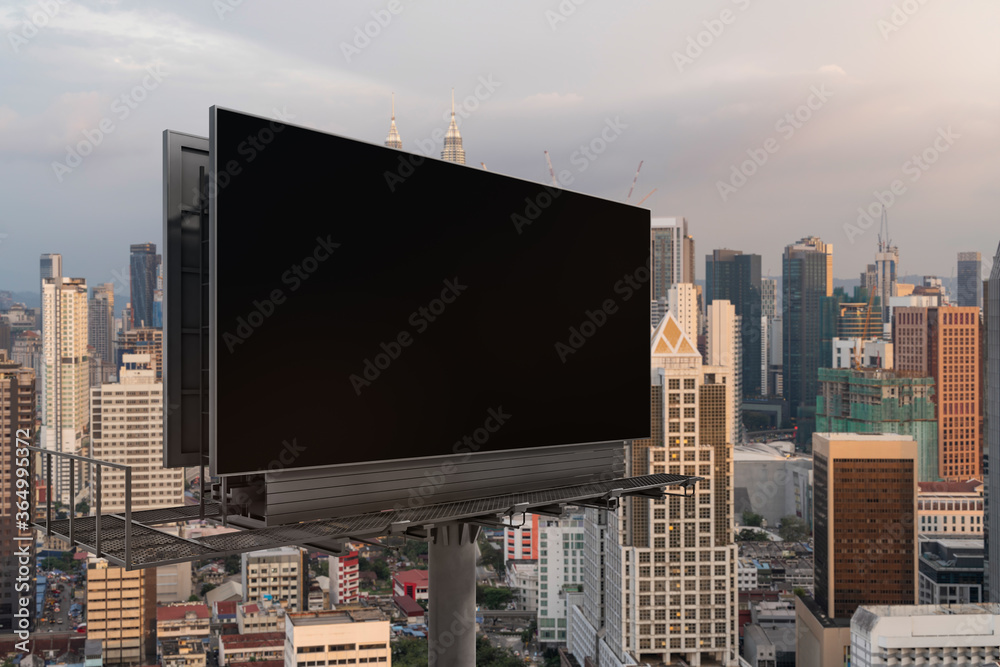 Blank black road billboard with KL cityscape background at sunset. Street advertising poster, mock up, 3D rendering. Side view. The concept of marketing communication to promote or sell idea.