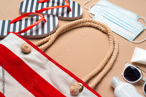 Beach bag with beach items and protective mask on beige background. Coronavirus summer concept