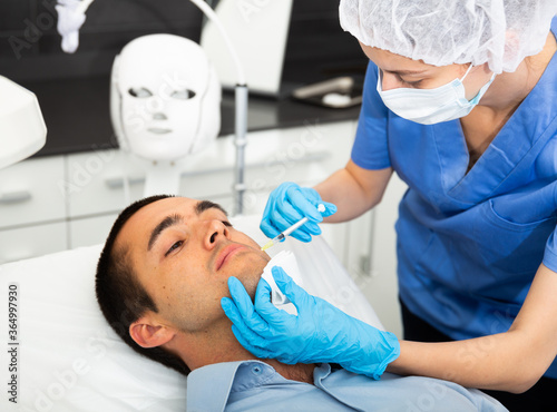 Young male patient getting injections for face skin tightening at aesthetic cosmetology clinic .