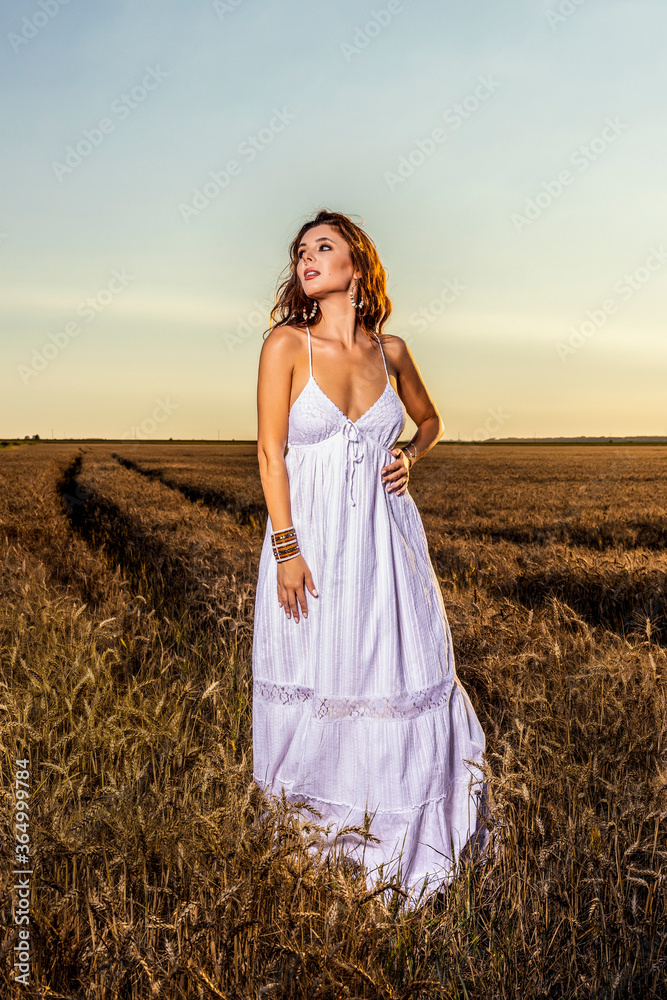 Obraz premium A beautiful woman in a white dress in a wheat field at sunset.