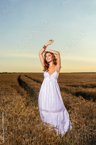A beautiful woman in a white dress in a wheat field at sunset.
