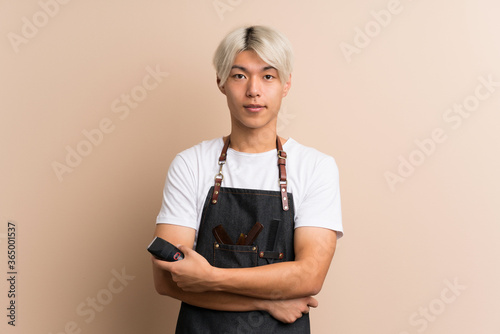 Young asian man over isolated background with hairdresser or barber dress and holding hair cutting machine photo