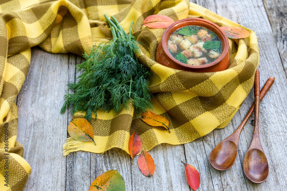Fototapeta premium Autumn soup with croutons and dill is warmed wrapped in a scarf with fallen yellow leaves lying around.
