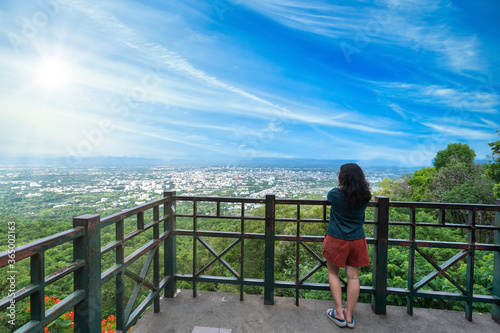 Asian Tourist hipster woman travelers looking with at admiring the view cityscape mountain range over the city air atmosphere bright blue sky background with white clouds of Chiang Mai,Thailand