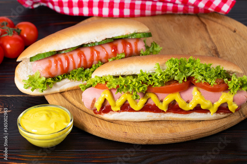 Hot dog with mustard, tomato and lettuce on wooden background