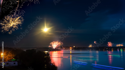 Fireworks over a lake with a full moon shining, lights reflected upon the water, shine the light.
