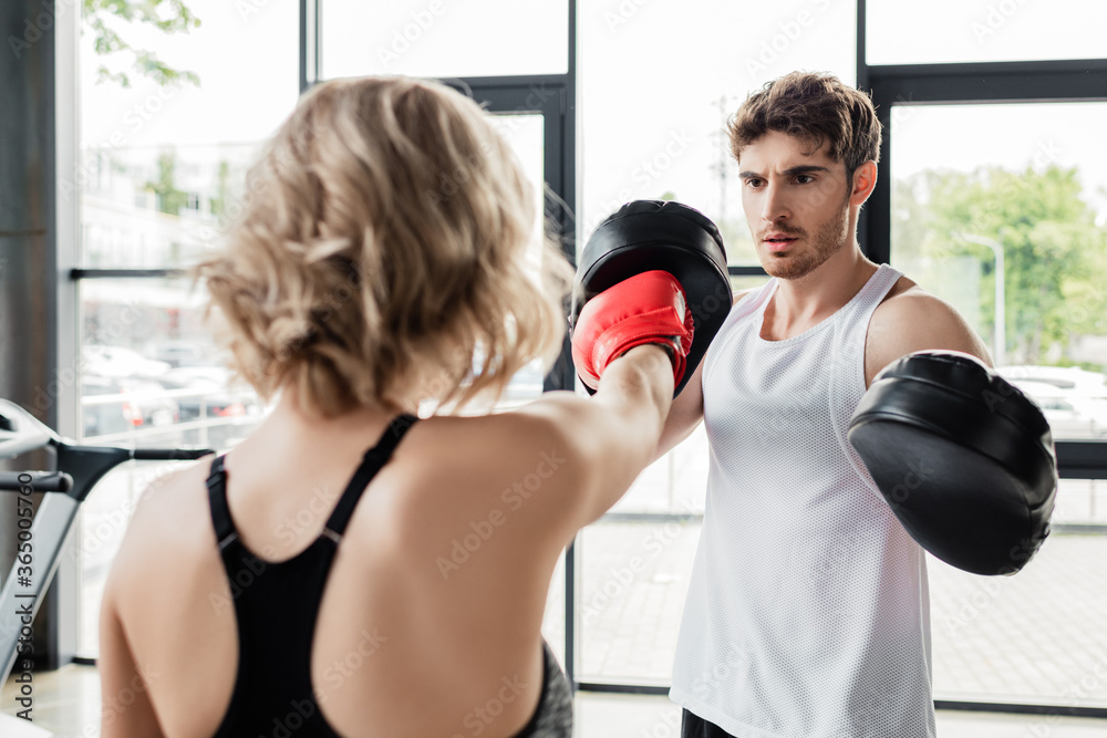 back view of sportive woman in boxing gloves exercising with man in boxing pads back view of sportive woman in boxing gloves exercising with man in boxing pads