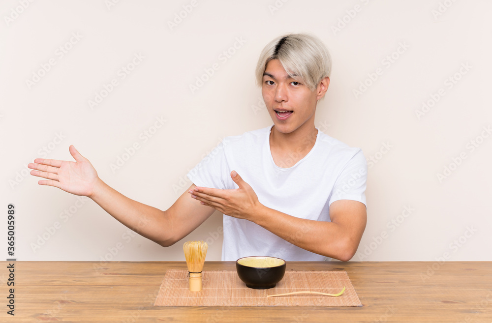 Young asian man with matcha tea in a table extending hands to the side for inviting to come Young asian man with matcha tea in a table extending hands to the side for inviting to come