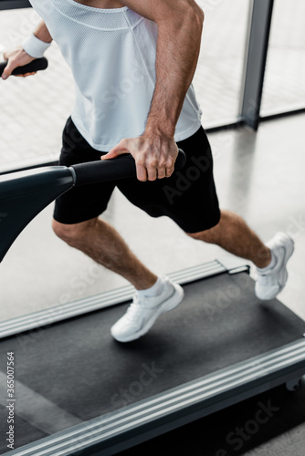 Принти на полотні cropped view of tired sportsman touching handrails on treadmill