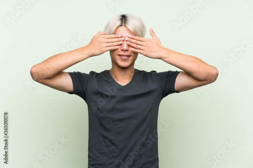 Young asian man over isolated green background covering eyes by hands