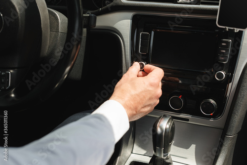 Cropped view of businessman adjusting vehicle audio system while driving car