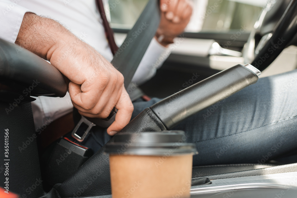 Selective focus of businessman fastening safety belt near paper cup in car