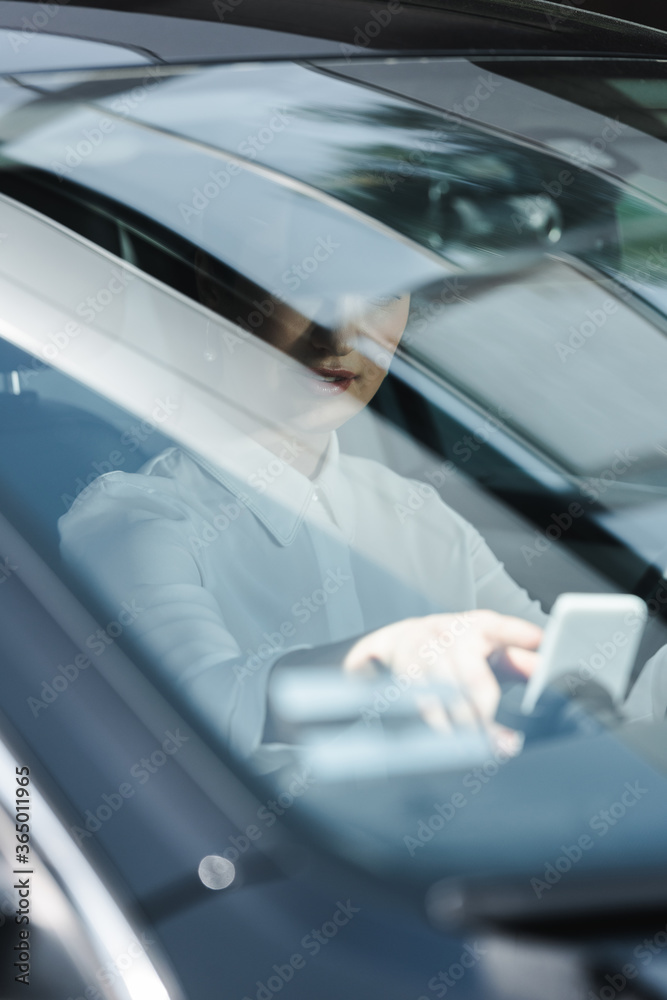 Selective focus of businesswoman using smartphone on driver seat in auto
