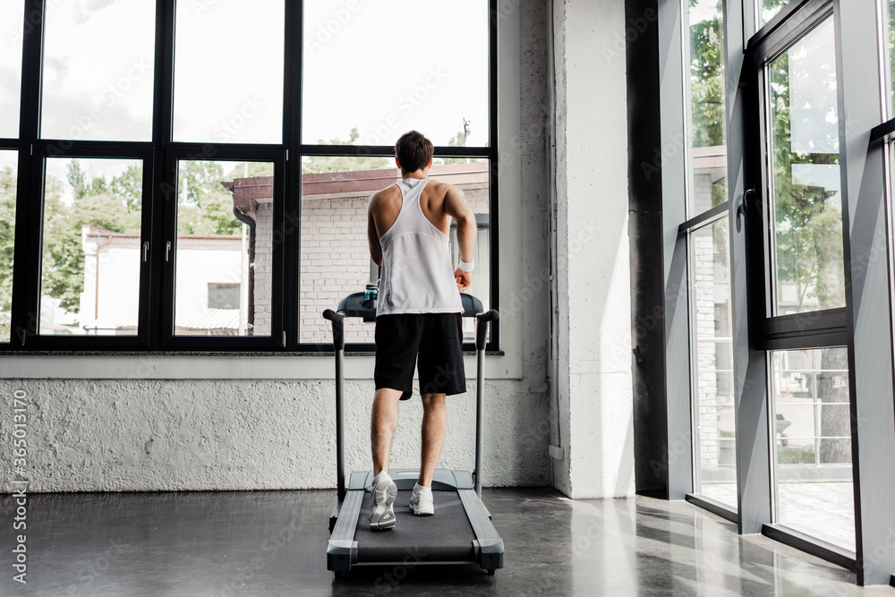 back view of man running on treadmill in gym