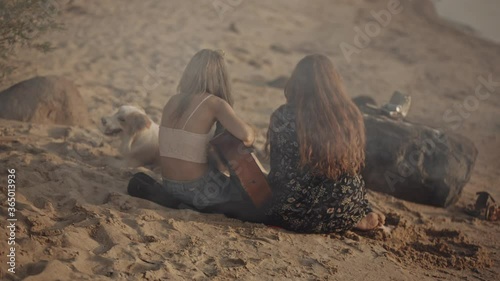 Vacation at sea with friends. Redhead and blonde hipster girl sitting on the beach singing and playing the guitar during sunset. Enjoying isolation together. Concets of friendship. travel, vacation. photo