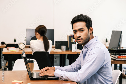 An Asian teenage man is sitting on a desk with a notebook. He is a company manager. he works hard to make the company successful.