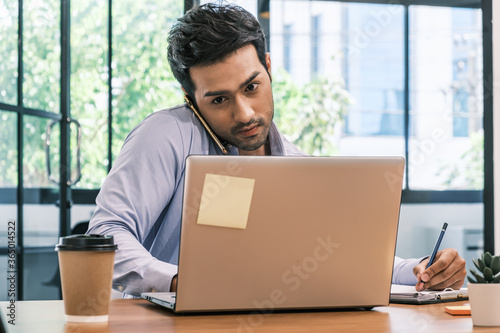 An Asian teenage man is sitting on a desk with a notebook. He is a company manager. he works hard to make the company successful.