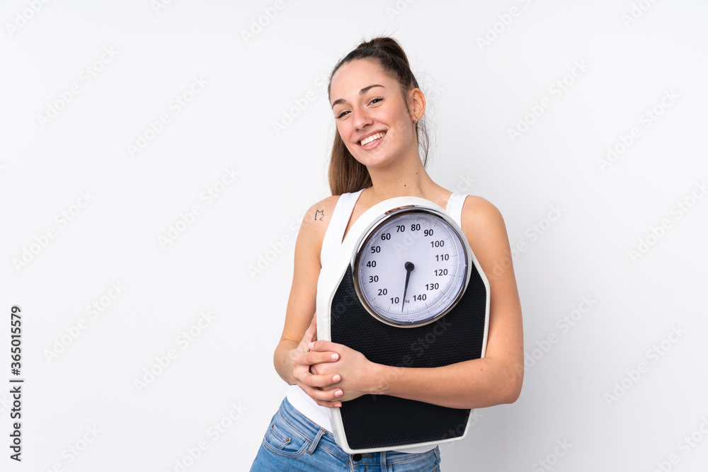 Young brunette woman over isolated white background with weighing machine Young brunette woman over isolated white background with weighing machine