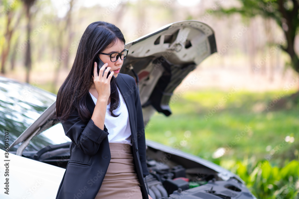 A young Asian woman is calling her service technician to fix a broken car on the side of the road
