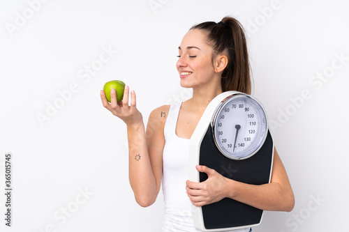 Young brunette woman over isolated white background with weighing machine and with an apple