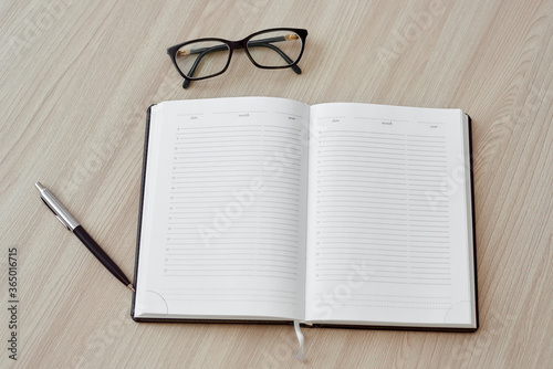 Open blank daily planner, pen, glasses on light wooden background. Top view