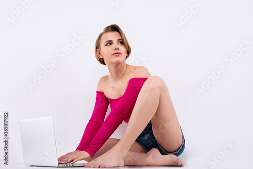 girl with long legs is typing on computer, young and beautiful girl works on Internet, white skin and short haircut, bright clothes