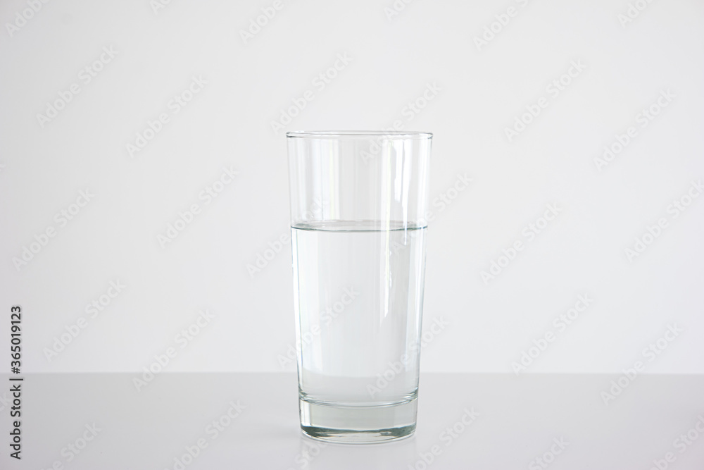Clear glass three quarters full of water set on white table isolated close up frontal shot Clear glass three quarters full of water set on white table isolated close up frontal shot
