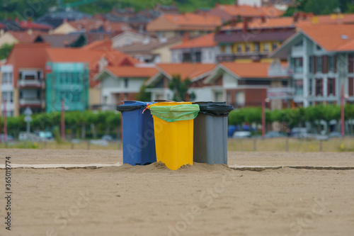 Street trash bins for separate garbage collection. Blue, yellow and gray waste bins. European small town citysape as background. Photography at the sandy beach. photo