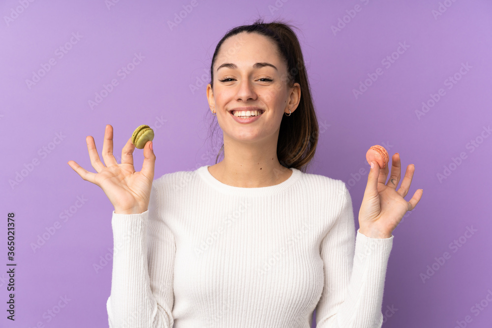 Young brunette woman over isolated purple background holding colorful French macarons Young brunette woman over isolated purple background holding colorful French macarons