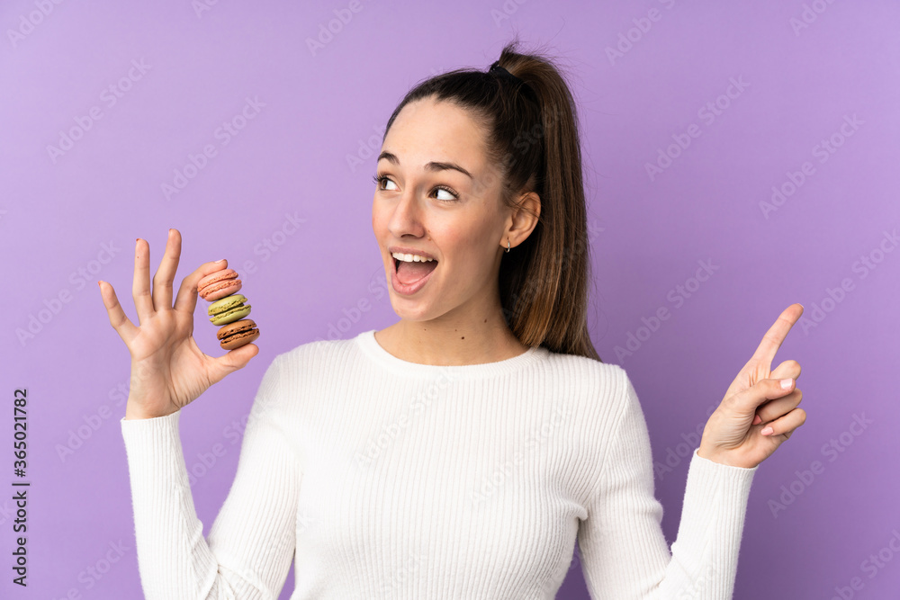 Young brunette woman over isolated purple background holding colorful French macarons and intending to realizes the solution Young brunette woman over isolated purple background holding colorful French macarons and intending to realizes the solution