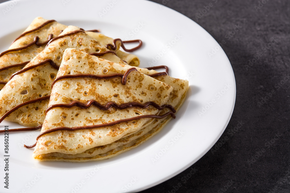 Sweet crepes with chocolate on black background