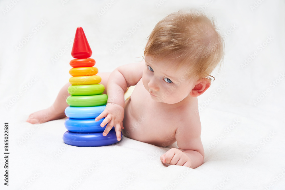 cute baby plays with a multi-colored toy pyramid on a light background cute baby plays with a multi-colored toy pyramid on a light background