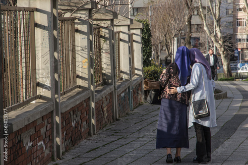 Two muslim young girls, standing and gossiping, in the shadows, next to a fence on the street. Or are they actually old catholic nuns? A concept of contradictions in religions and optical illusions. photo