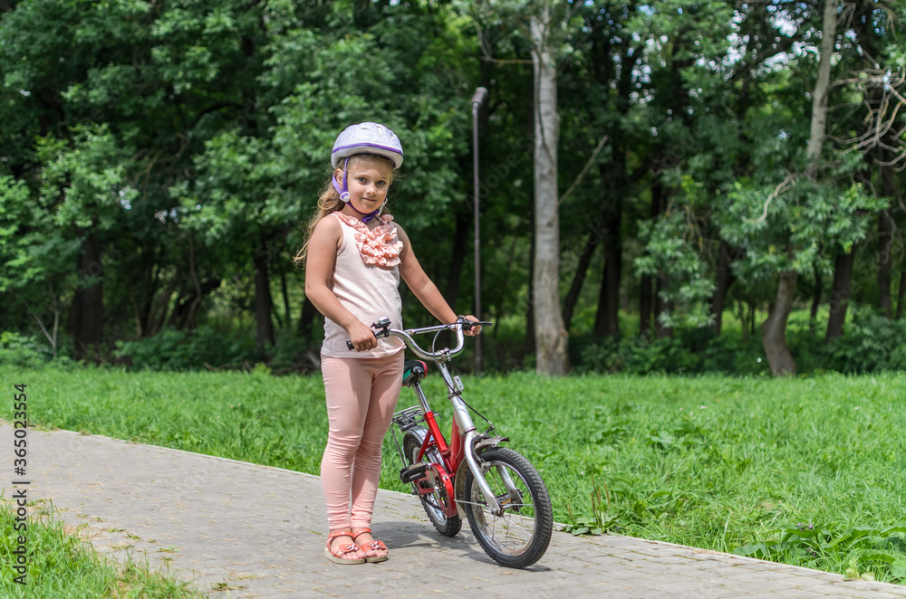 Little charming girl in a bicycle helmet rides a bicycle in the park Little charming girl in a bicycle helmet rides a bicycle in the park