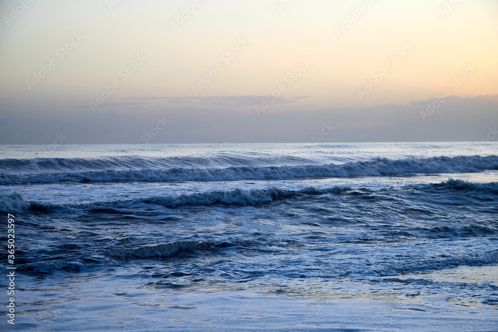 Water of sea with waves and yellow sky at sunset.