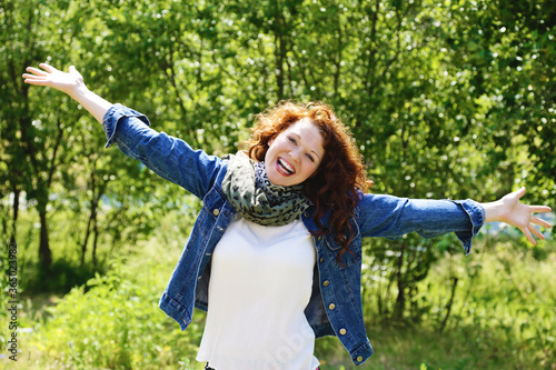 jeune et jolie femme rousse aux longs cheveux bouclés souriant et pleine de joie de vivre dans un parc ensoleillé en été  photo