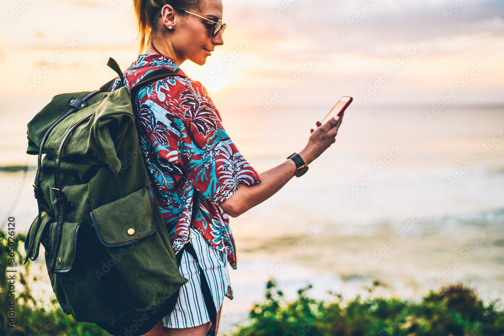 Back view of attractive positive woman tourist in sunglasses having video call with friends via smartphone application and 4G internet.Cropped image of traveler enjoying summer vacation near to ocean