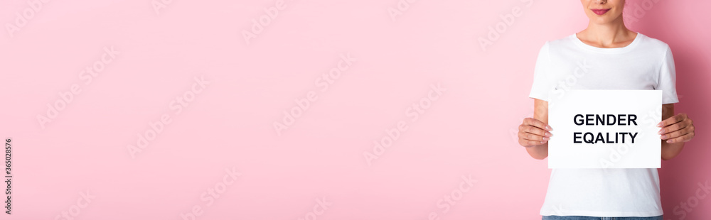 panoramic crop of woman in white t-shirt holding placard with gender equality lettering on pink panoramic crop of woman in white t-shirt holding placard with gender equality lettering on pink