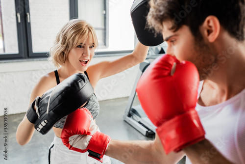 selective focus of emotional sportswoman in boxing pads exercising with man in gym