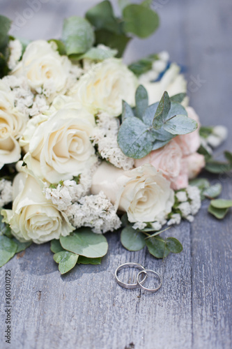 wedding rings and bouquet of white roses on wooden table